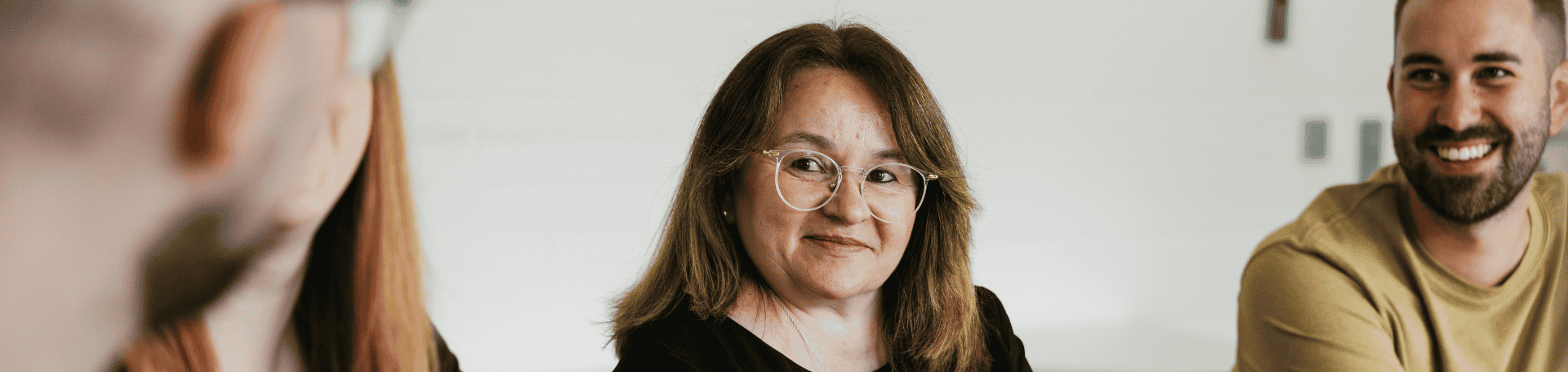 Frau mit Brille sitzt lächelnd in Gesprächsrunde, flankiert von Kollegen rechts und links.