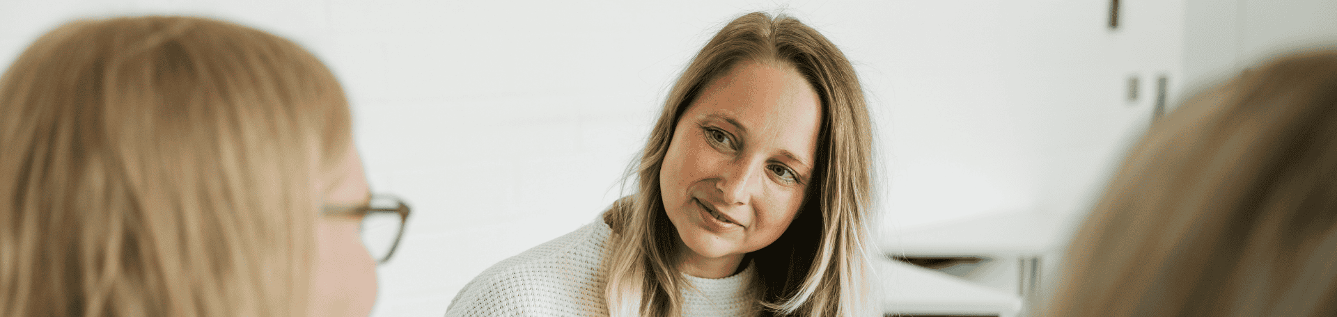 Frau mit langem blondem Haar hört zwei Kolleginnen aufmerksam zu.