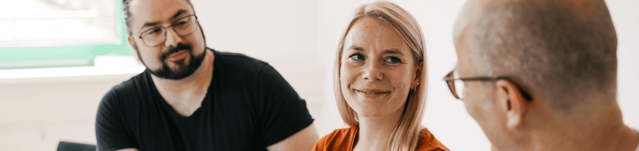 Zwei Männer und eine Frau sitzen am Tisch und unterhalten sich freundlich.