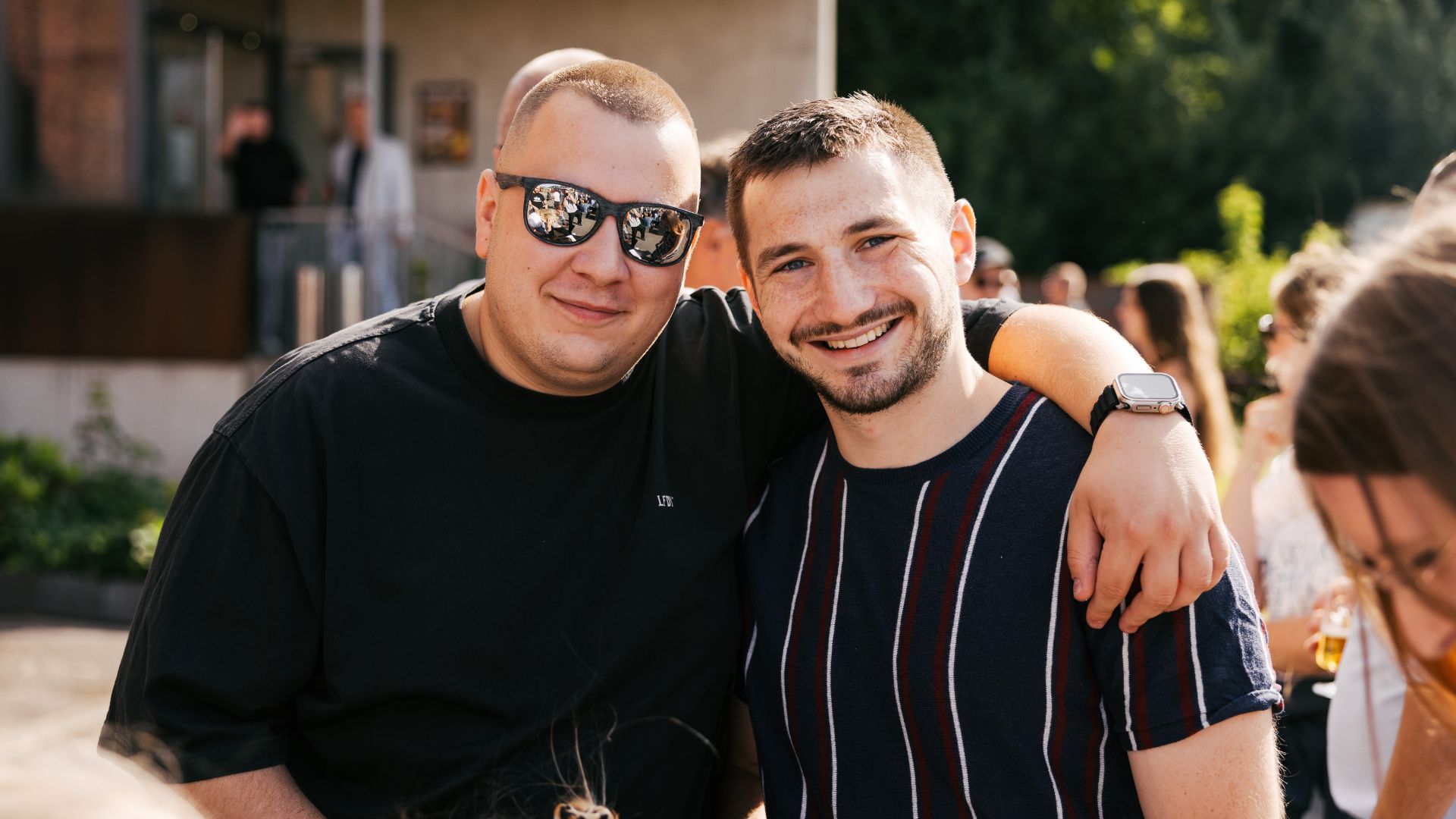 Zwei Personen, einer mit Sonnenbrille schauen lächelnd in die Kamera. 