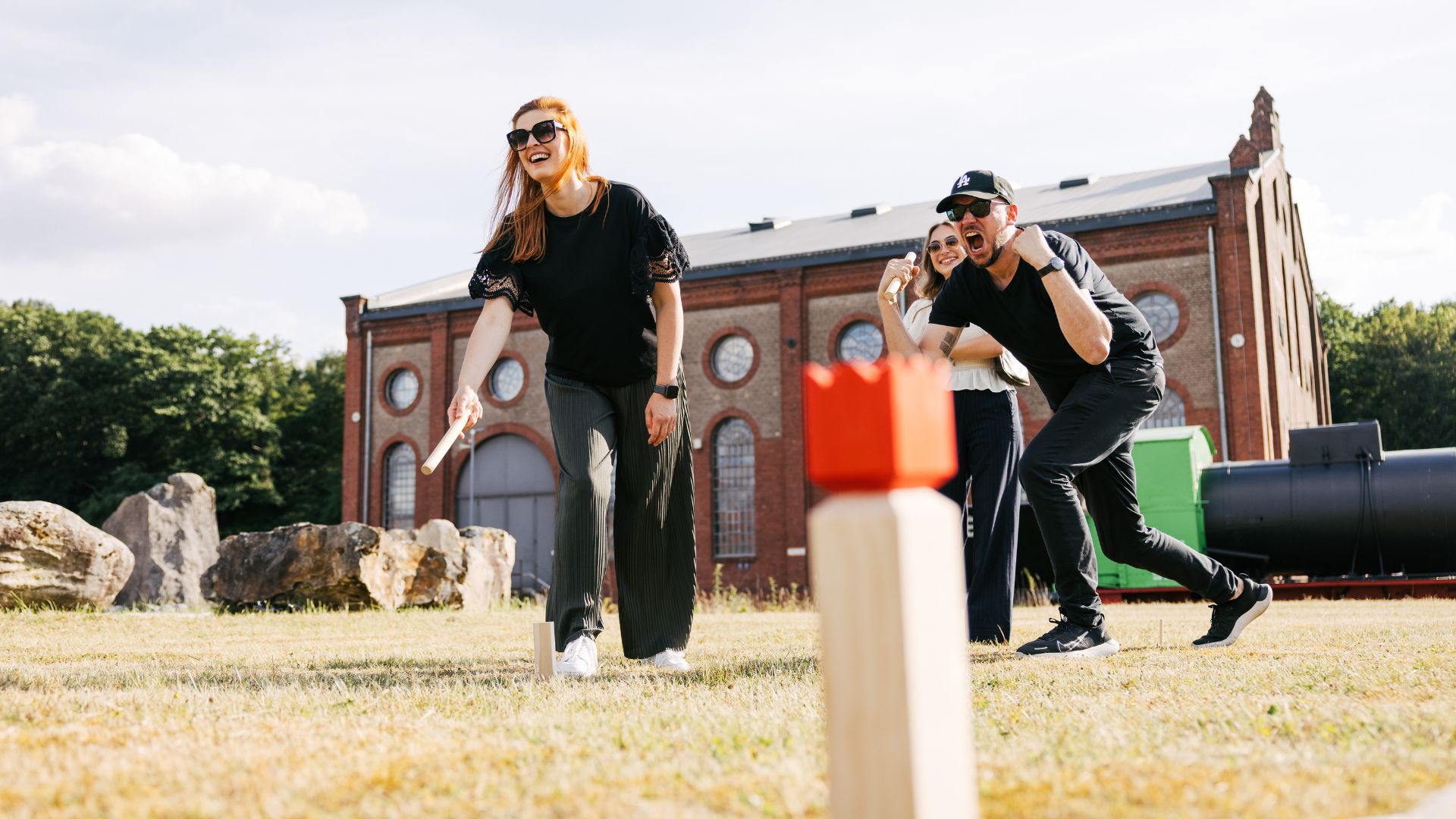 VEDA-Mitarbeiter:innen spielen Kubb. Ein Mitarbeiter feuert seine Kollegin energisch an.