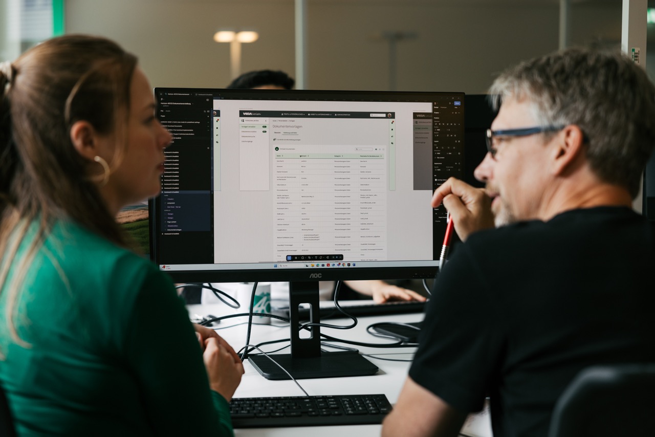Zwei VEDA-Mitarbeiter:innen sitzen gemeinsam vor einem UX-Design und tauschen sich aus.