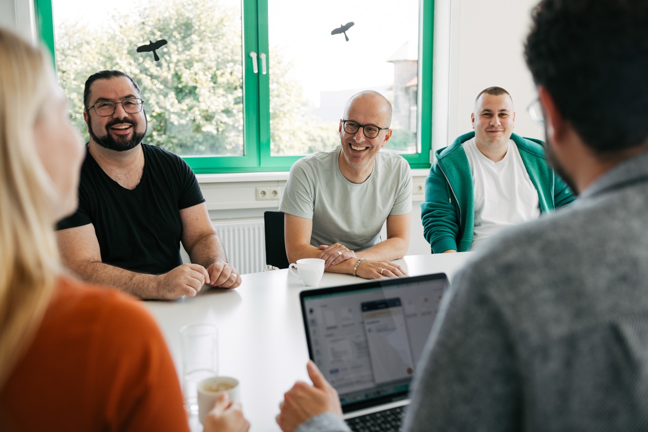 Teammitglieder sitzen gemeinsam an einem Tisch und lachen während eines Meetings.