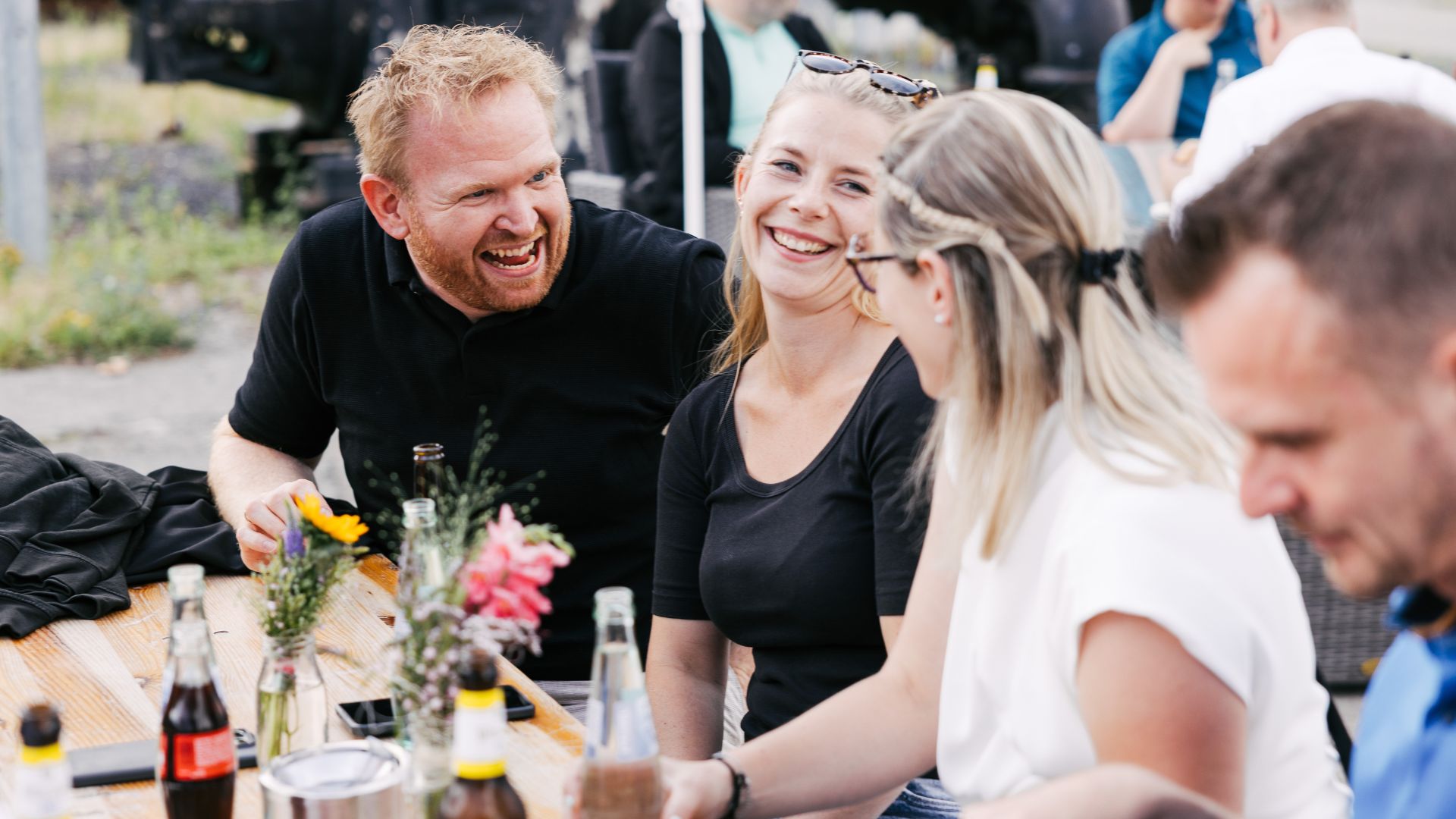 VEDA-Kolleg:innen sitzen am Tisch lachen zusammen beim Sommerfest.